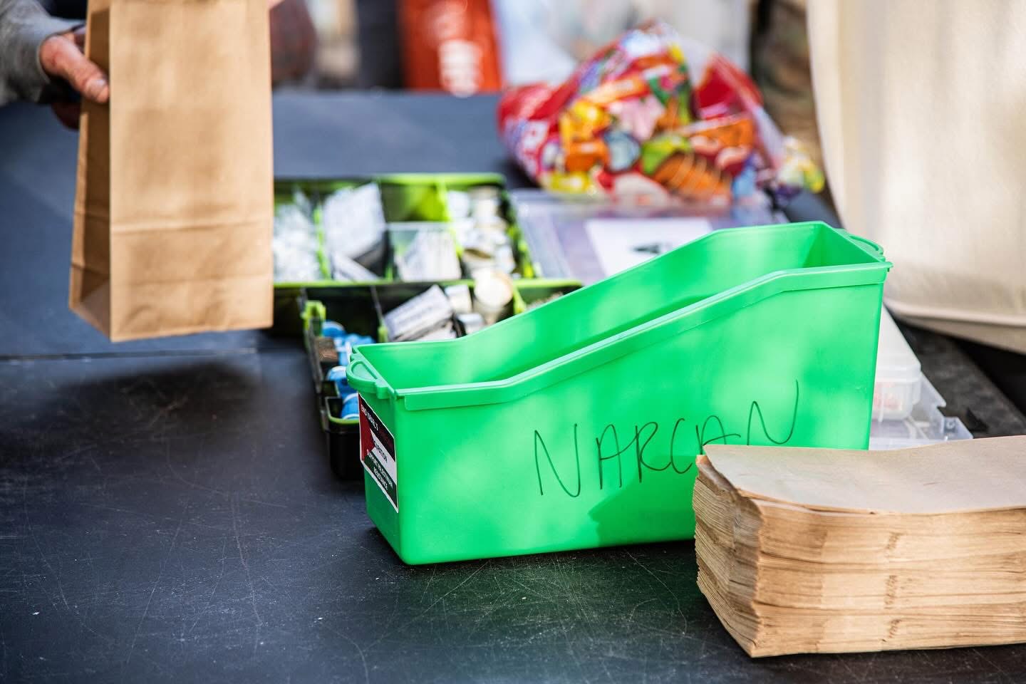 A green bin labeled Narcan next to paper bags